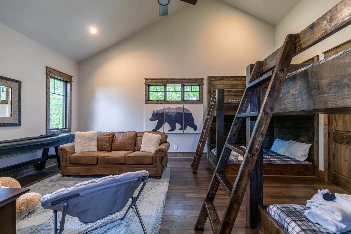 A playful, family-oriented interior featuring bunk beds, a cozy brown leather couch, bear-themed wall art, and a wooden table set up for games. The relaxed, welcoming space is designed for gathering, playing, and family bonding after a day of outdoor fun.