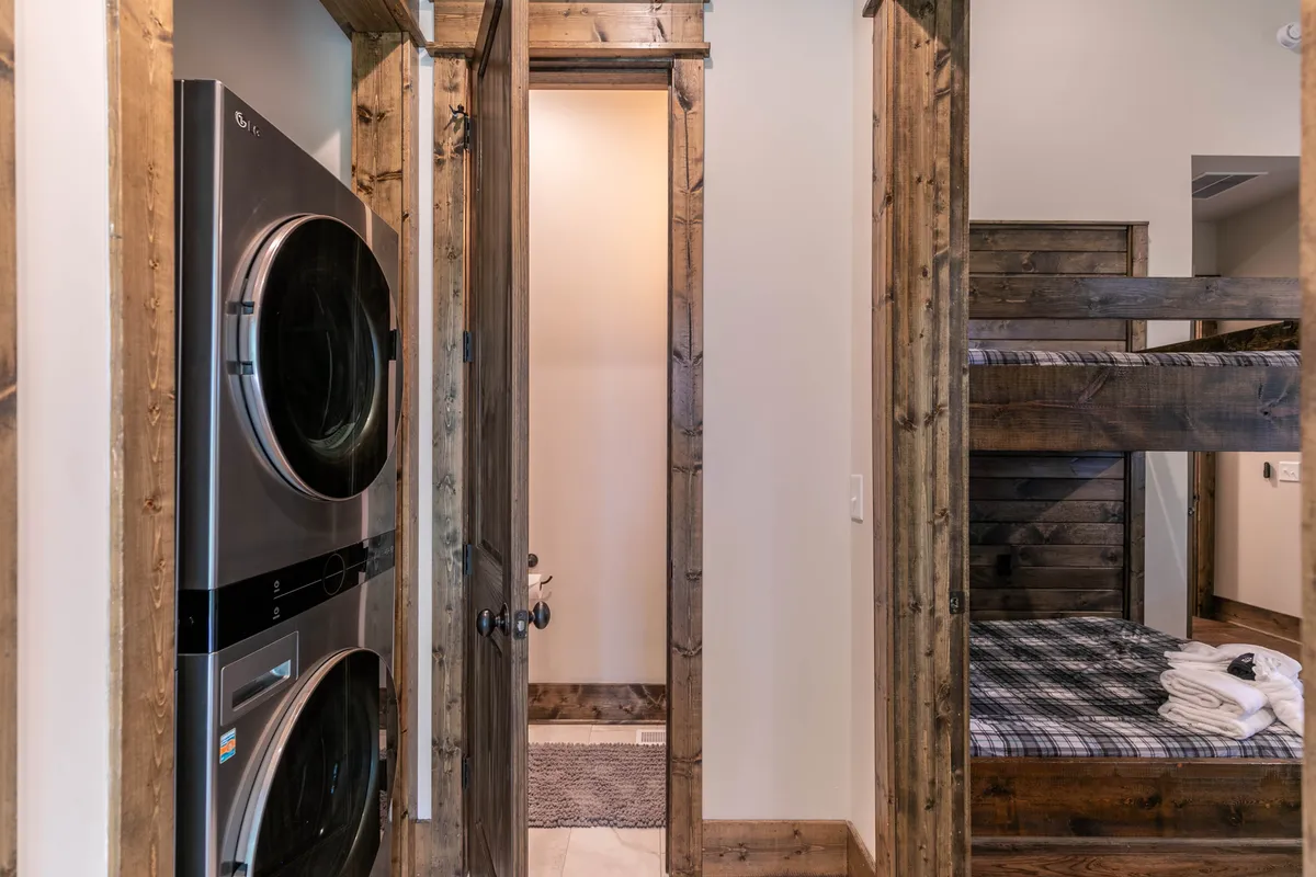 A practical and inviting bunk room with stacked bunk beds and a washer/dryer. The room is well-lit and features cozy bedding, making it especially appealing for families or groups with children.