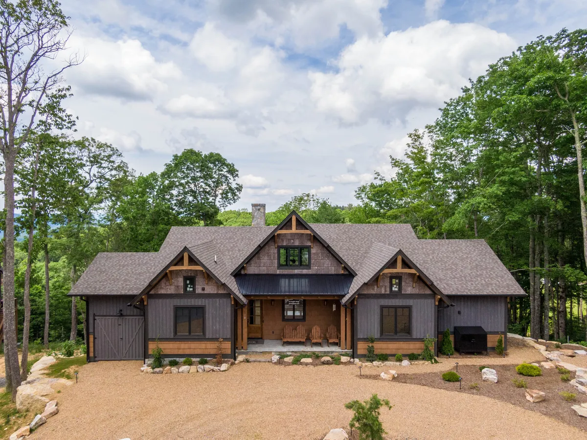 A welcoming front porch with rocking chairs set against a landscaped garden and lush trees, highlighting the architectural charm of the property and its connection to the outdoors.