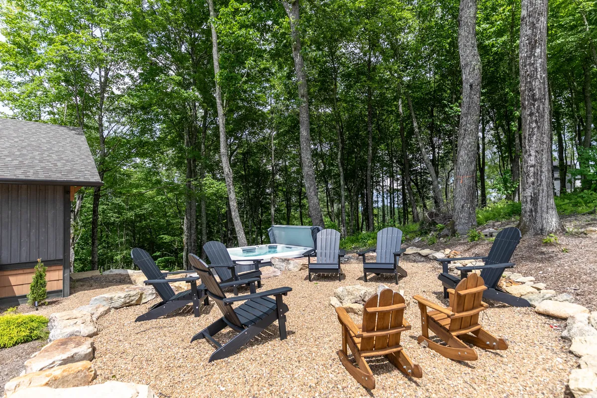 A landscaped outdoor area with a cozy seating arrangement and a hot tub nestled among the trees. The ambiance is warm and inviting, ideal for social gatherings, relaxation, or enjoying sunset views through the branches.