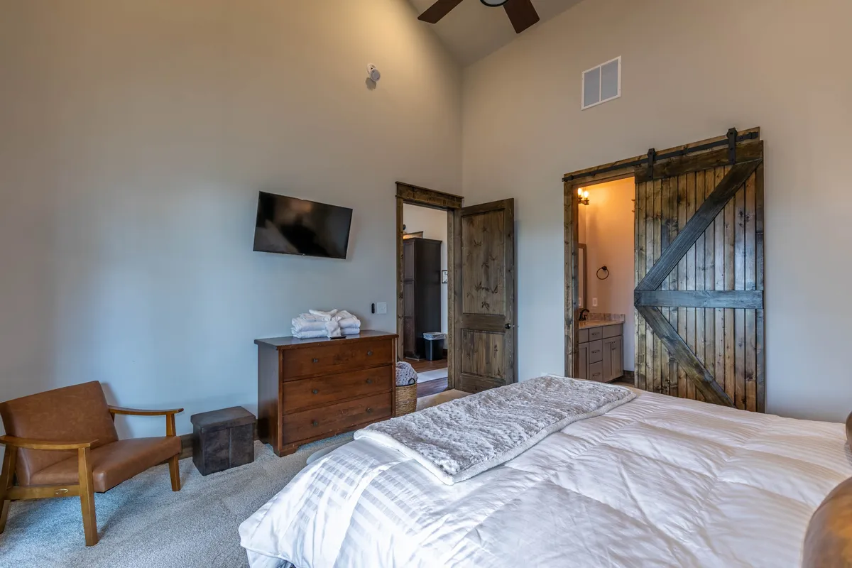 A cozy bedroom with a bed dressed in textured bedding, complemented by a wooden dresser and sliding barn-style door. The soft lighting and tasteful decor create an atmosphere of comfort and quiet escape.