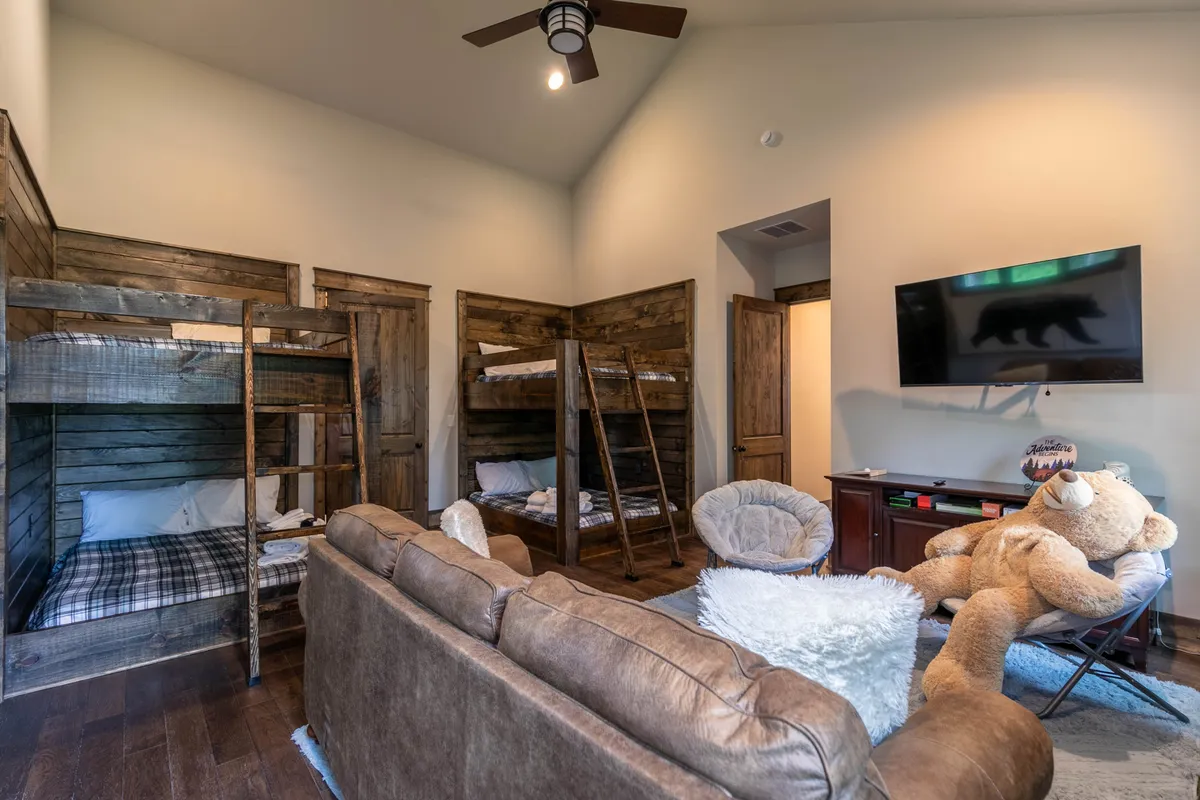 A cheerful kids' room with multiple bunk beds, a giant teddy bear, a comfortable seating area, and a TV—perfect for sleepovers and family movie nights. The mood is fun and inviting, emphasizing group enjoyment.