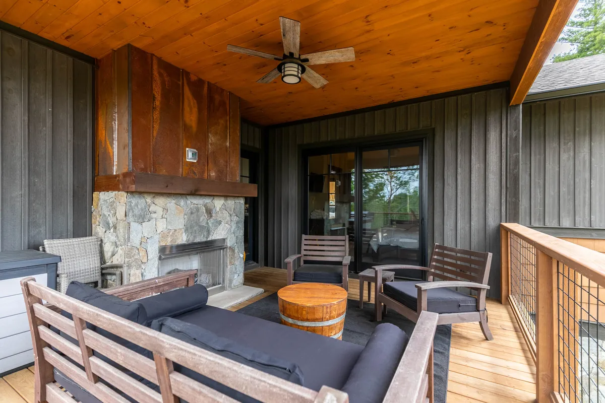 A welcoming deck scene featuring a gas fireplace as the centerpiece, complemented by a cozy seating arrangement and a wooden ceiling overhead. The space exudes comfort and encourages relaxation or gathering with friends, with the fireplace ready for use as the sun sets behind scenic mountain peaks.
